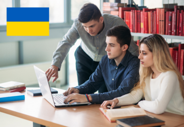 Three students sit in front of the laptop in a library. In the picture is the Ukrainian flag. ©gritsivoleksandr