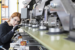 A red-haired woman wearing safety glasses checks something on a machine© FACC/Bartsch