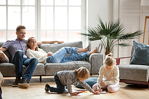 Young parents sit on a couch in the living room and watch their two children play© iStock/fizkes