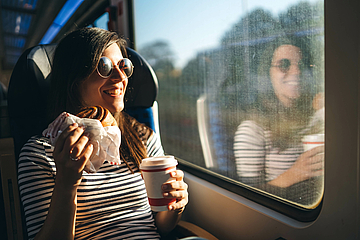 Young woman in sunglasses sitting on a train laughing © iStock/urbazon